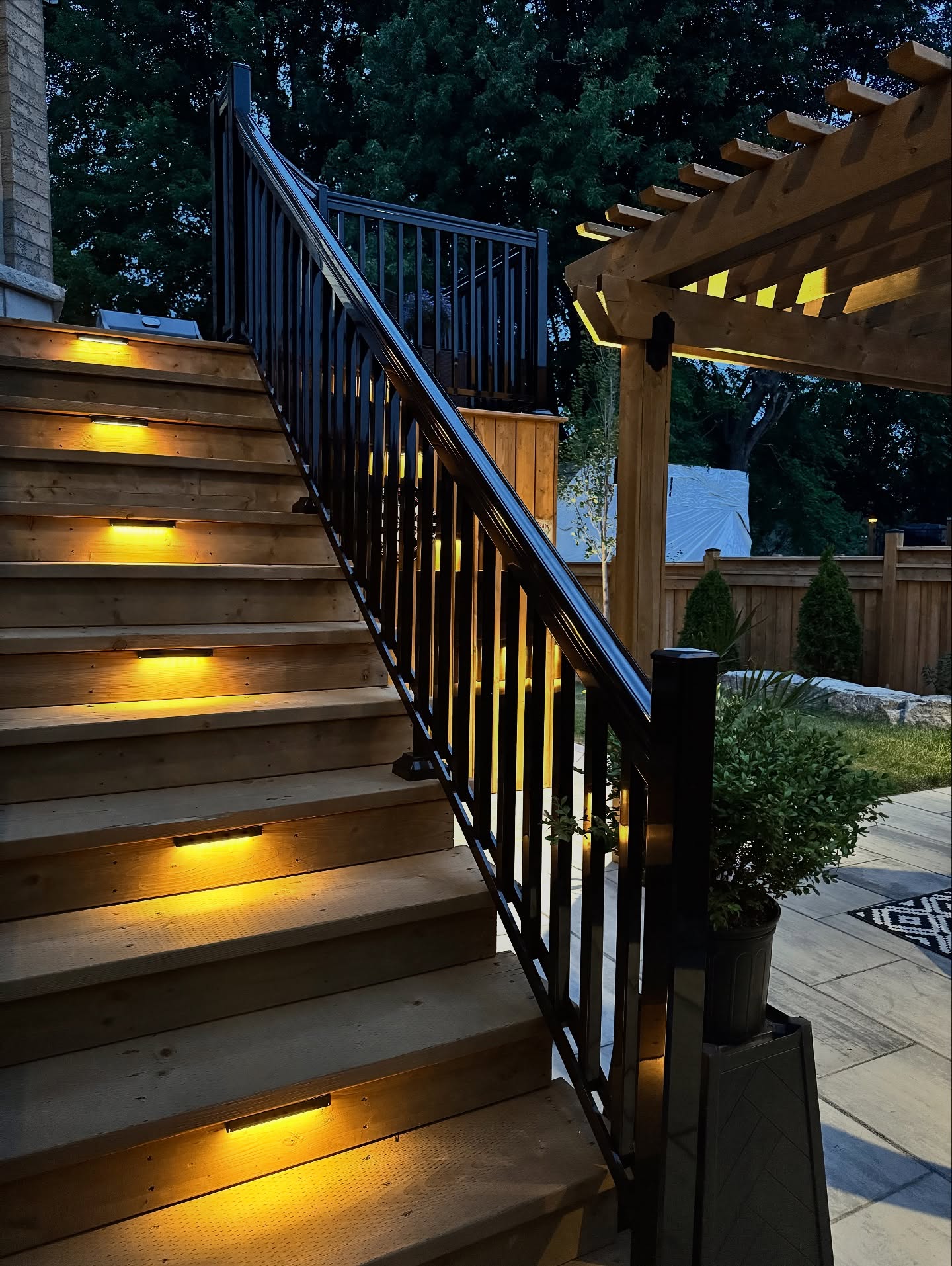 Cedar deck stairs with recessed step lighting and black aluminum railing at dusk