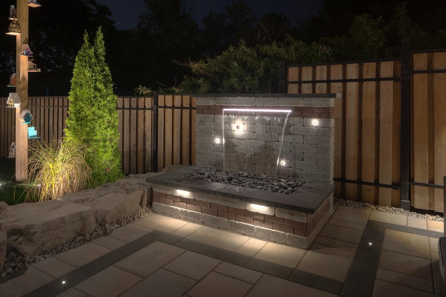 Illuminated stone waterfall feature with river rock basin at night