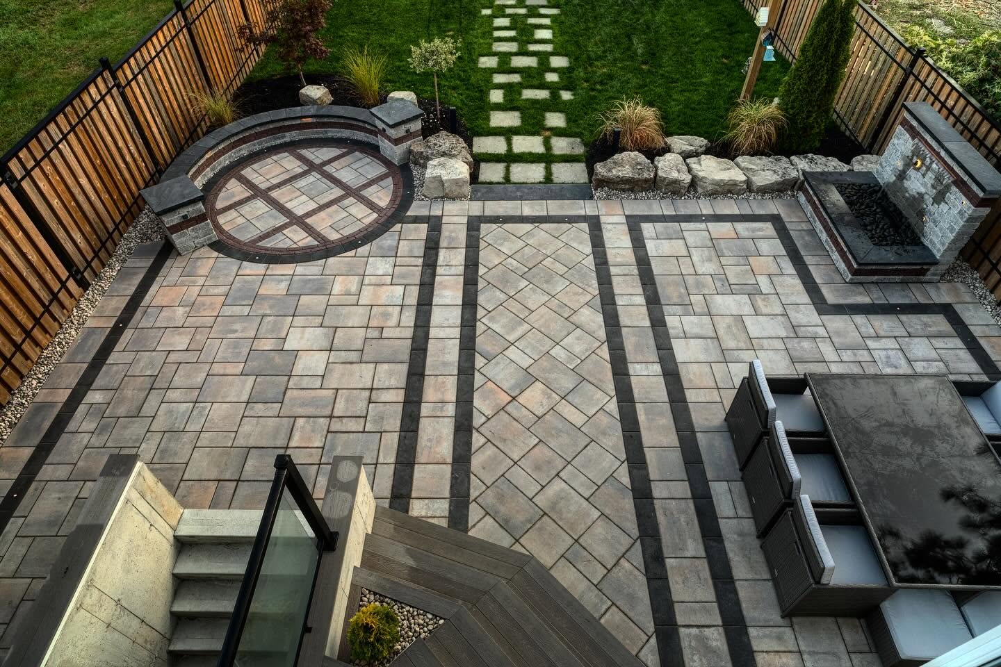 Aerial view of a paver patio with circular fire pit seating area and stone fire feature