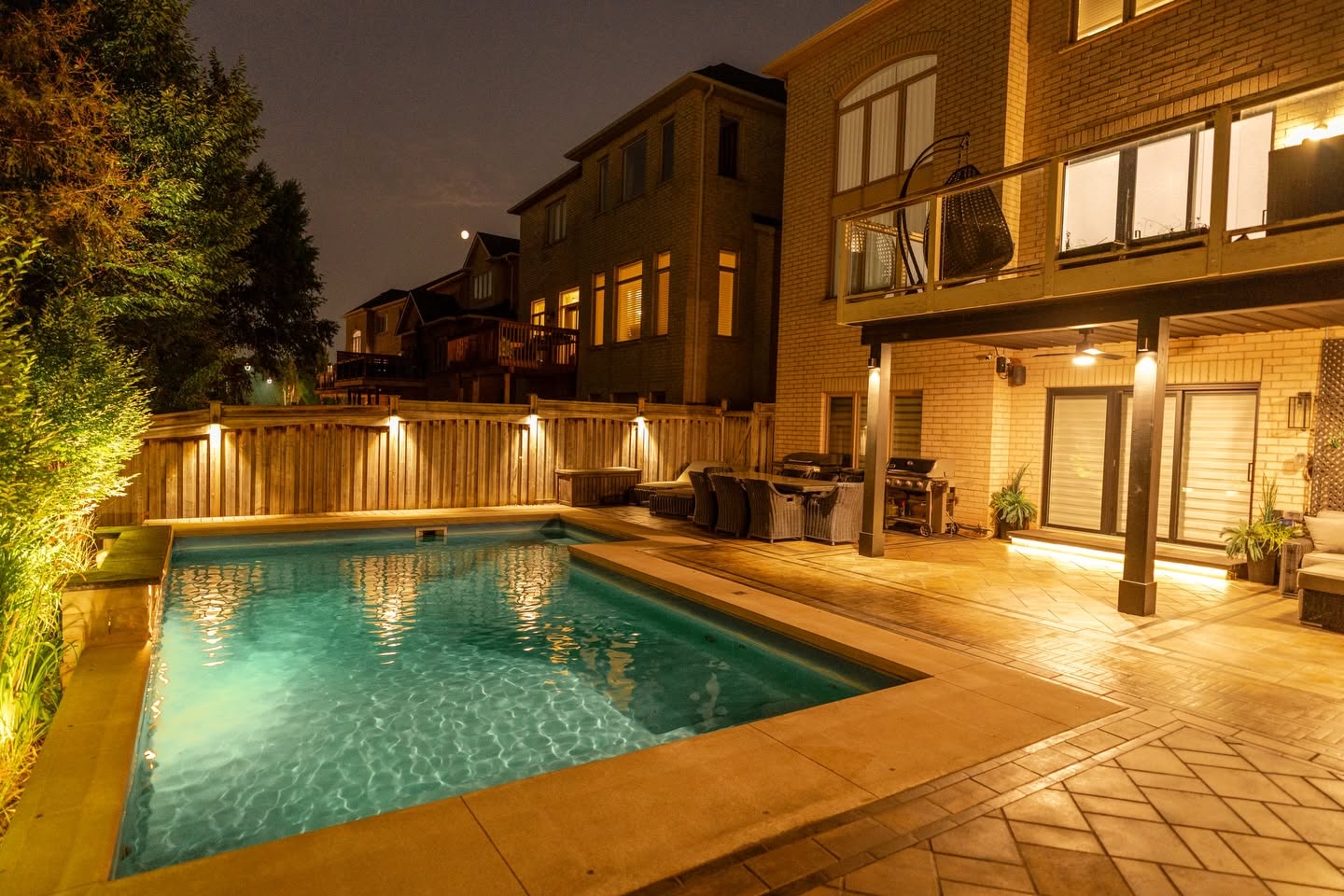 Backyard pool and patio lit at night by MADDA-WORX landscape lighting